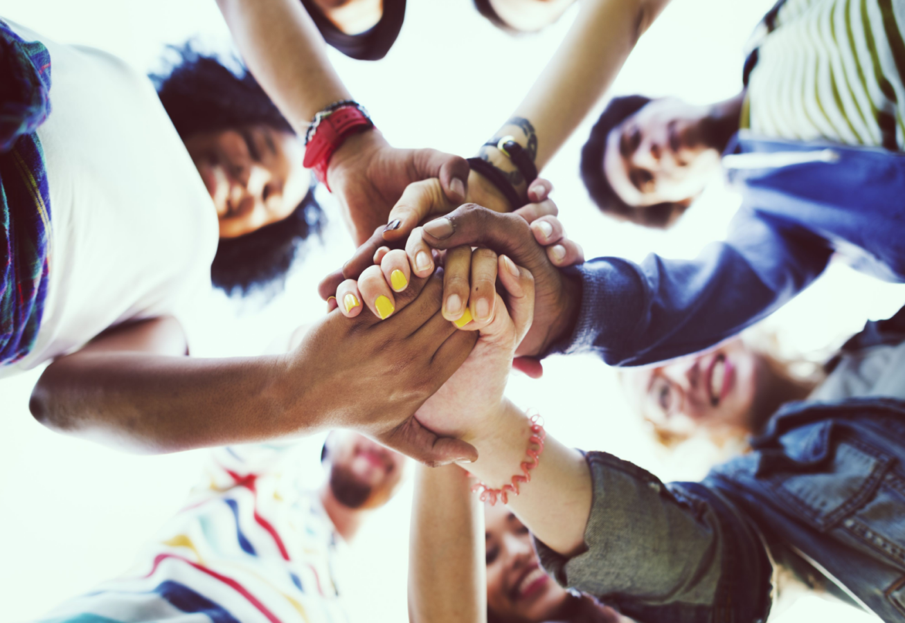 Photo of a ring of people all grasping hands in the middle. The view is taken from underneath.