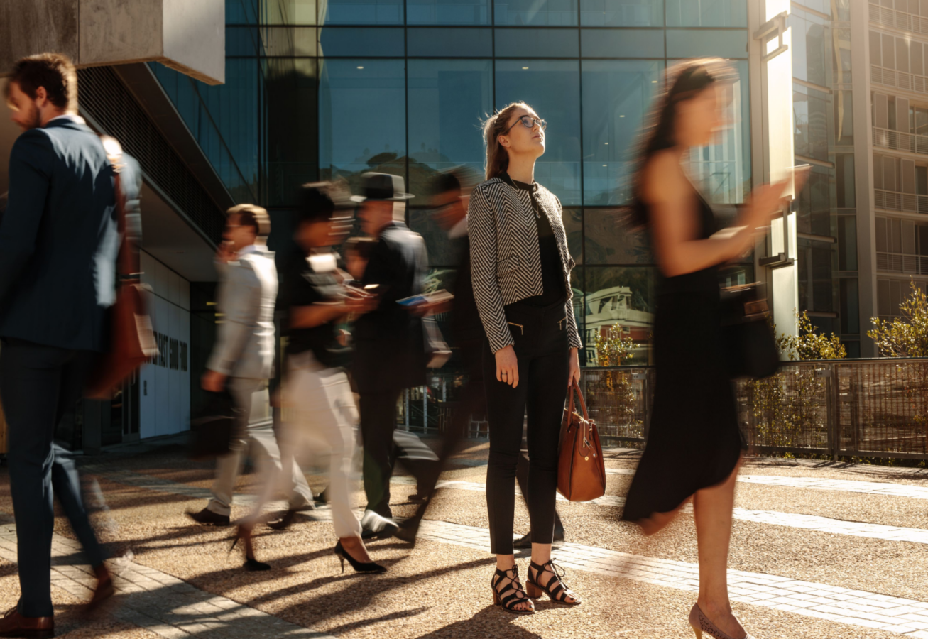 Photo of a business woman who has stopped to think, while others pass her by.